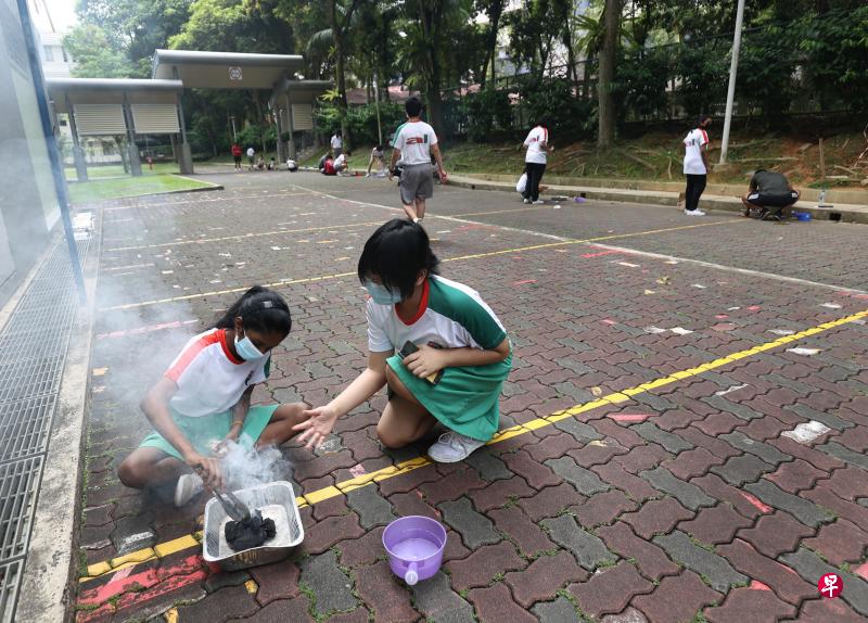 中二学生李小米（13岁，右）和雨佳（Yugathisswary D/O Krisnan，14岁，左）是好朋友，两人经过一番努力终于把火炭点燃。老师也为每组学生备好额外水源，一旦发生意外，能及时浇灭火源。（陈渊庄摄）