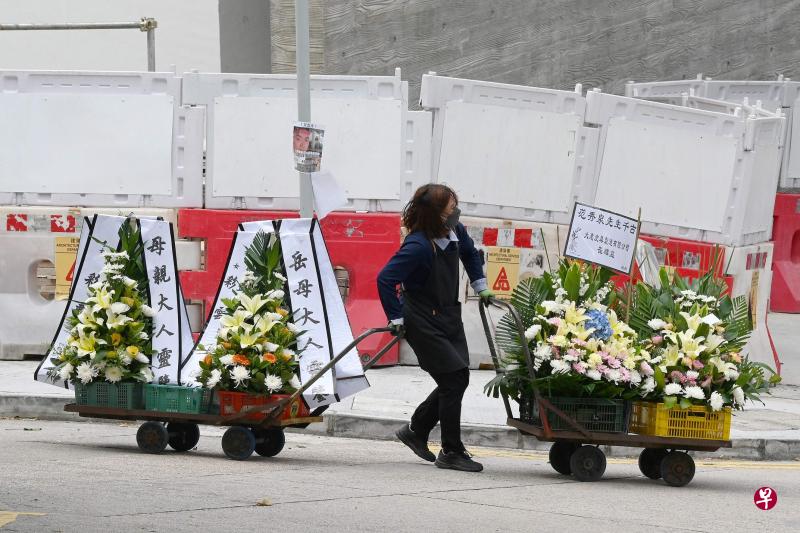 香港第五波冠病疫情造成最近每日都有超过百人不治，死亡人数激增导致殓房“爆满”。图为一名女职员昨天在位于新界大围的富山公众殓房，忙着用两辆推车运送祭奠逝者的花圈。（法新社）