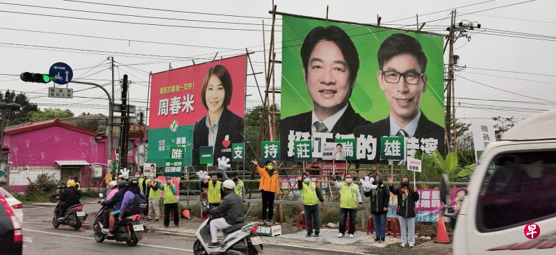 台湾屏东内埔乡的十字路口，挂着两幅巨大的选举看板，有台湾副总统赖清德支持的钟佳滨，也有当过法官的大热门周春米，两人都来自民进党最大派系新潮流。英系候选人庄瑞雄（橙色外套挥手者）卡上一脚，率队向上班民众挥手拜票。（温伟中摄）