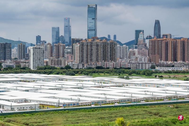 香港实施“逆向隔离”检疫安排的地点初步首选邻近深圳的落马洲河套区。这里有北京今年5月援建竣工的方舱设施，含约4500个独立房间及逾1万张床，落成至今尚未使用。图为方舱设施和不远处的深圳市景。（彭博社）