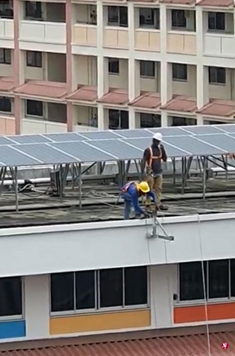 两名在组屋屋顶安装吊架的工人，身上的安全背带没有扣在固定装置上。（作者提供）