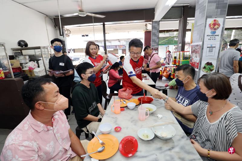 依斯干达公主城候选人刘镇东到新山大学城的咖啡店拉票，与正在用餐的民众握手致意，背后派发宣传单的是民行党柔佛再也州议员廖彩彤（红衣者）。（邝启聪摄）