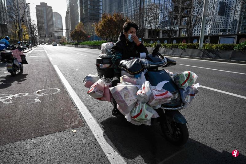 北京封控区域持续增加，多地出现囤货潮，导致送货平台配送压力骤增，一度出现骑手紧缺、送货时间延长等情况。图为11月25日一名行驶在北京街头的外卖骑手。（法新社）