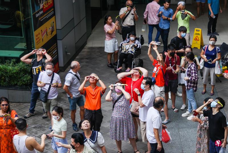 新加坡路边天文组织在大巴窑中心外的空地举行日食观测活动，向路过的公众分发日食观测眼镜，并讲解相关的天文知识。在可观测到日偏食的最后10多分钟，太阳渐渐“露面”，不少公众驻足尝试观看。（白艳琳摄）