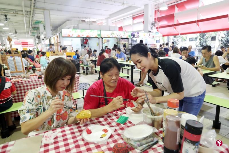 公众刘兴梅（中）今早跟儿子到茨园小贩中心吃早餐，碰巧遇到现场正主办美术活动，她跟卫生部兼环境及水源部高级政务部长许连碹（左）一起替食物模型上色。（饶进礼摄）