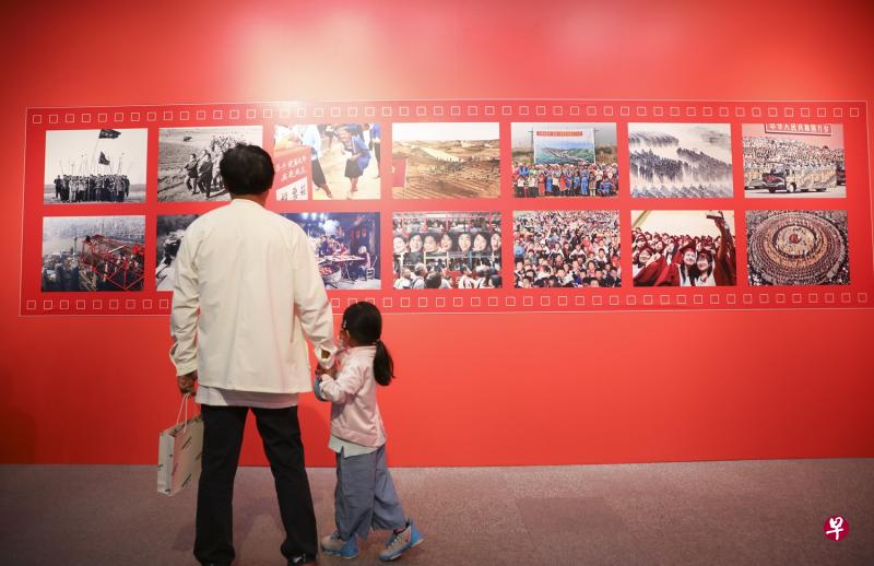 一老一小不久前在北京参观《百名摄影师聚焦新中国70年》图片巡展。该展览展出百名摄影师的作品，展现了中国70年来的发展成就与民生变迁。（中新社）