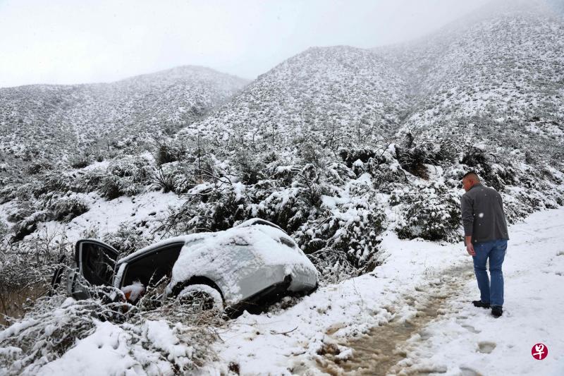 南加州暴风雪持续，已致超过12万人家中停电，当地多条公路的多个路段关闭，以及数十架航班取消。图为南加州绿谷（Green Valley）附近一段公路遭暴雪袭击，一辆轿车打滑栽进池塘。（法新社） 